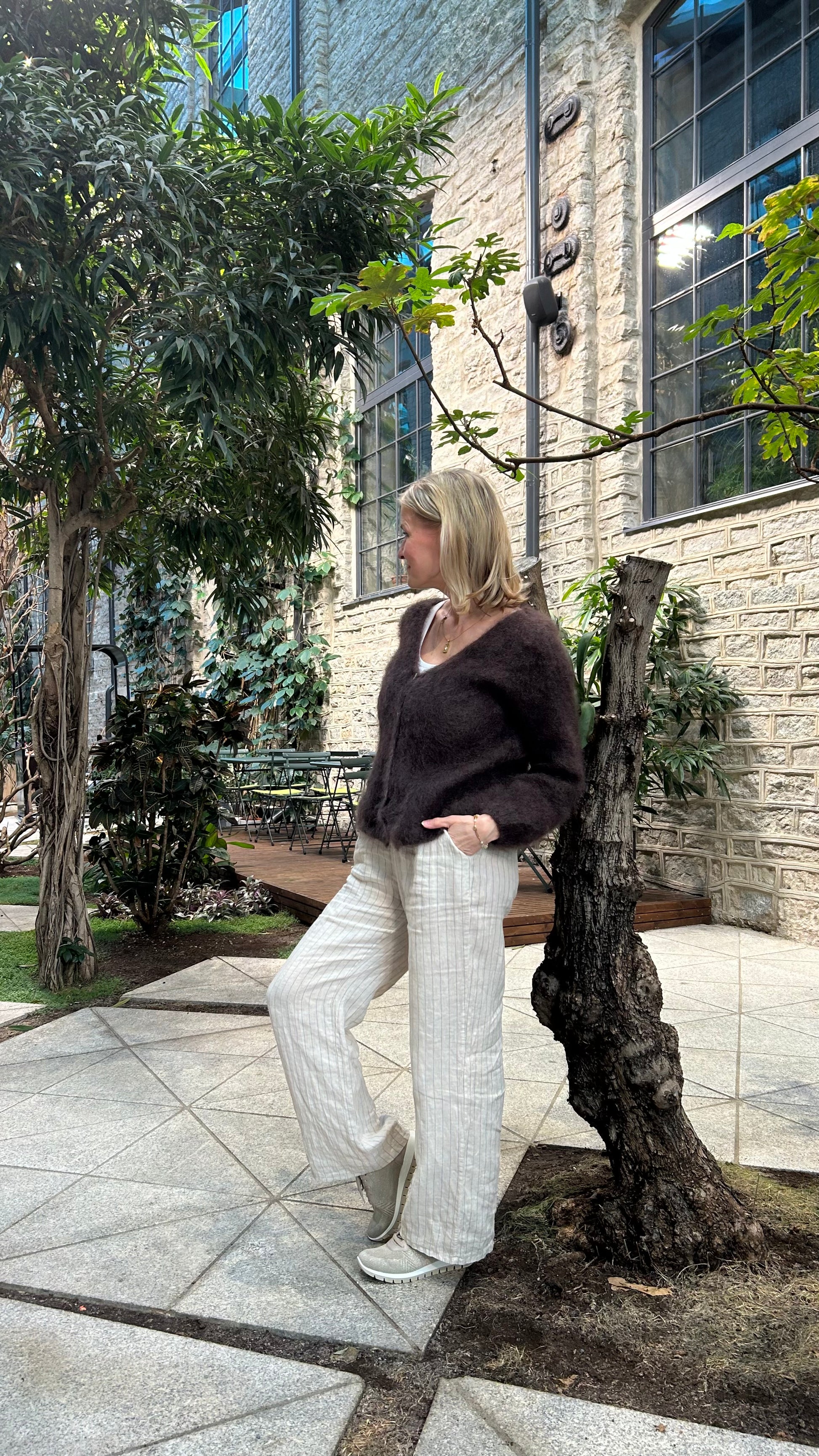 Women wearing brown kid mohair cardigan with beige linen pants leaning on a three